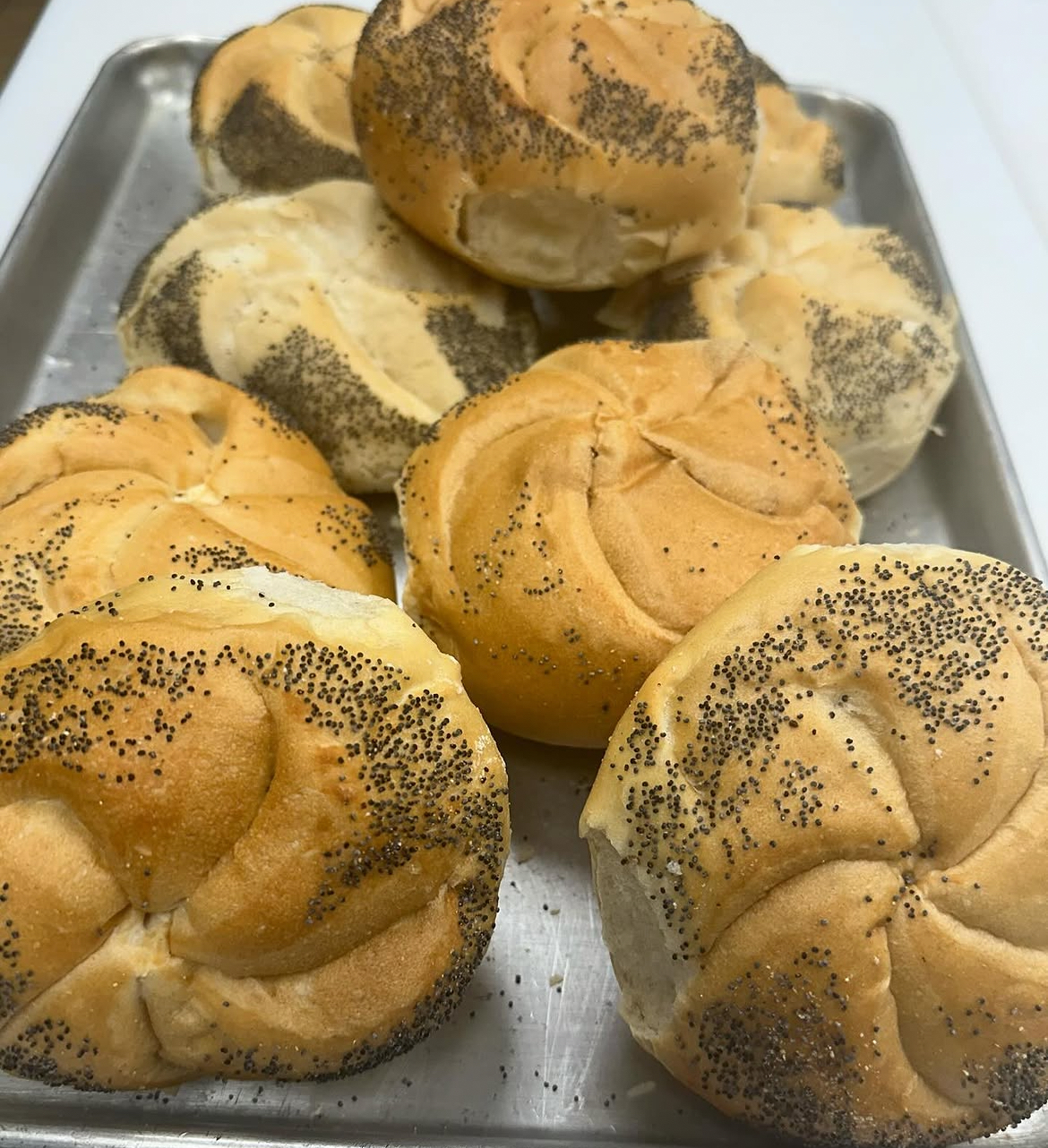 Fresh-baked poppy seed kaiser rolls on a sheet tray