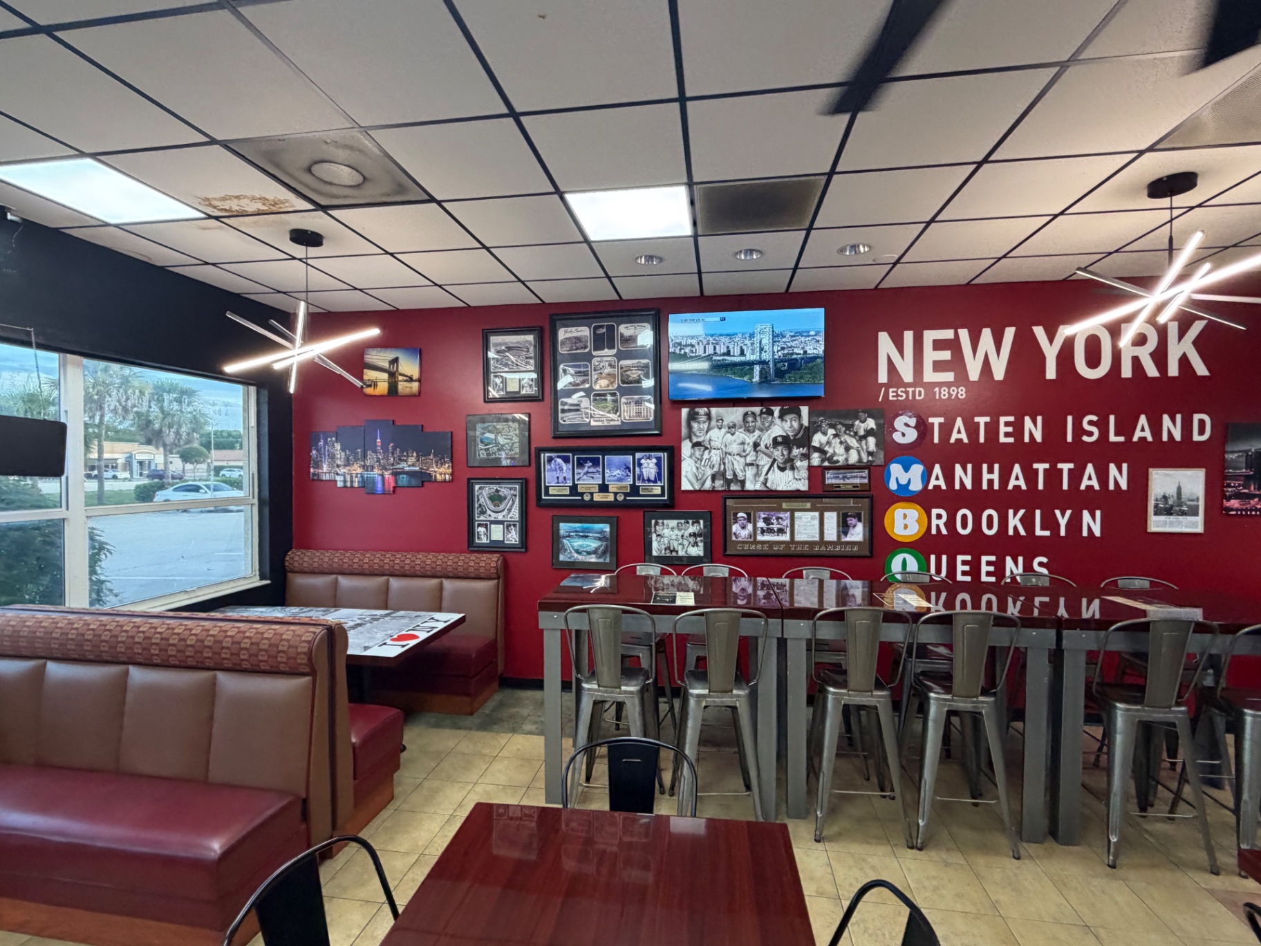Inside Breakfast Bros NY Cafe — red walls, leather booths, NY subway letters and framed Yankees photos
