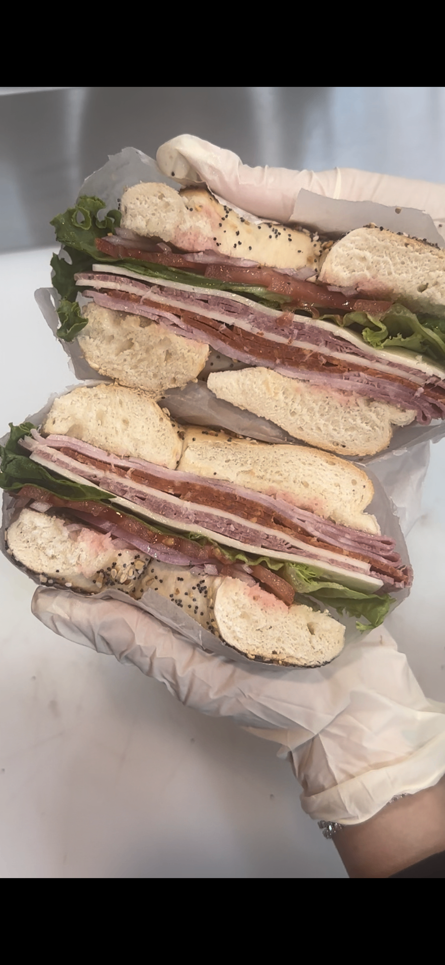 Two ultimate bagel sandwiches stacked with ham, salami, provolone, lettuce and tomato