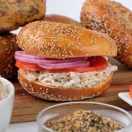 Tuna salad on a sesame bagel with tomato and red onion